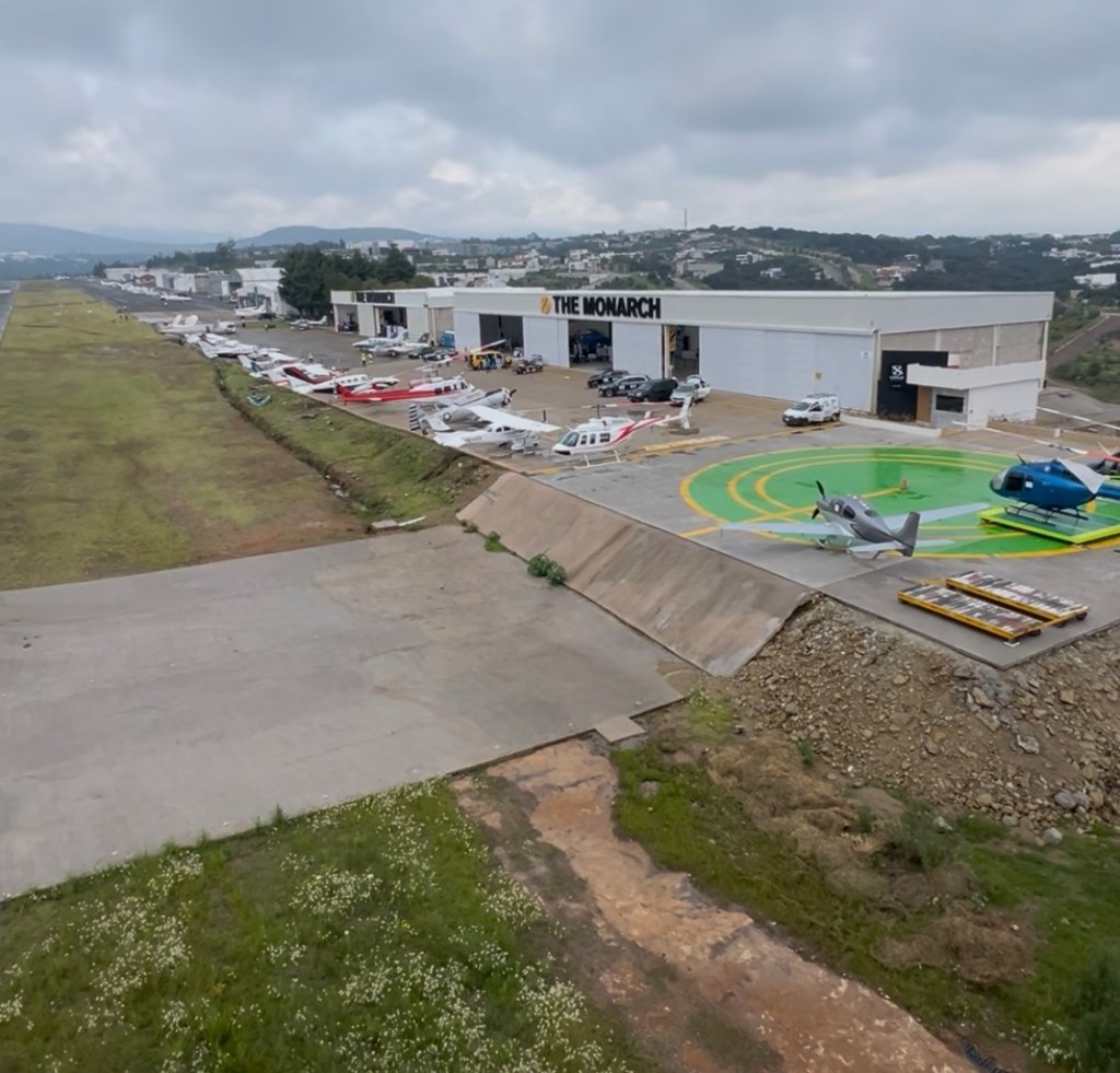 Vista panorámica del hangar y helipuerto de THE MONARCH, con varias aeronaves estacionadas y áreas verdes en el entorno.